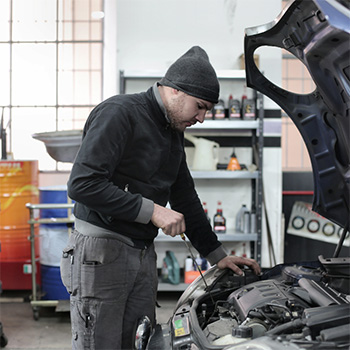 Mechanic wearing a beanie inspecting a car's engine during engine repair in Gaithersburg, MD