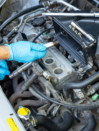 Gloved hands replacing a spark plug during car tune-up service.